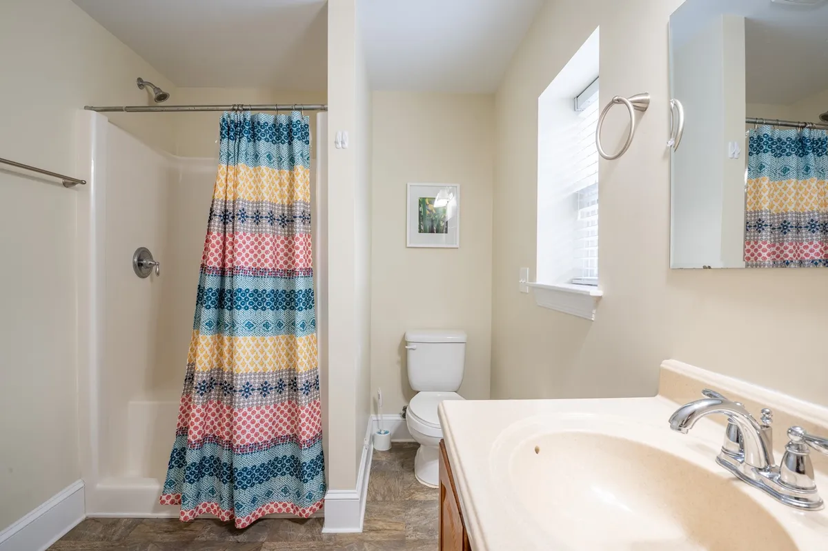 A cheerful bathroom scene with a colorful shower curtain, a single vanity featuring a countertop, and a wall-mounted mirror. The space is bright and inviting, ideal for refreshing morning or evening routines.