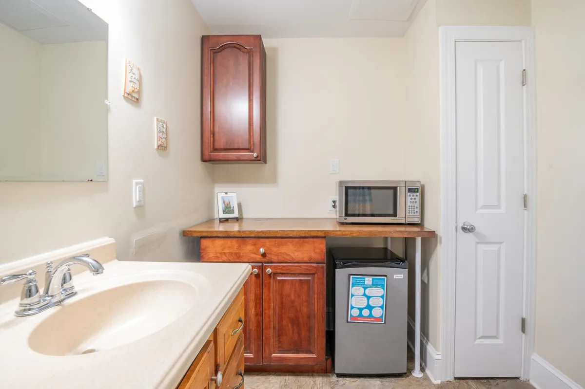 A cozy essentials nook featuring a wooden counter with a sink, a microwave, and a mini fridge. The setup is designed for convenient meal prep and quick snacks, with homey touches that create a welcoming atmosphere.