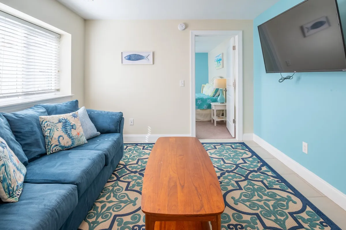 The photo captures a comfortable living area with a blue couch, wooden coffee table, textured area rug, wall art, and a television. The cozy atmosphere is enhanced by soft lighting and tasteful decor, inviting guests to relax, read, or enjoy entertainment together.