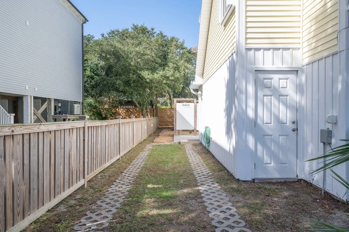 This image shows an inviting exterior view with a pathway leading to a doorway, a partially visible fence, and surrounding trees. The scene suggests a welcoming outdoor area perfect for walking with a pet or enjoying the outdoors together.