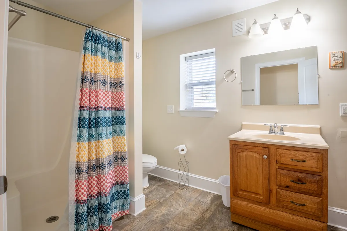 A well-lit bathroom interior featuring a vibrant shower curtain, wooden cabinetry under the vanity, and ample natural light. The fresh, inviting feel makes it perfect for both relaxing baths and quick morning routines.