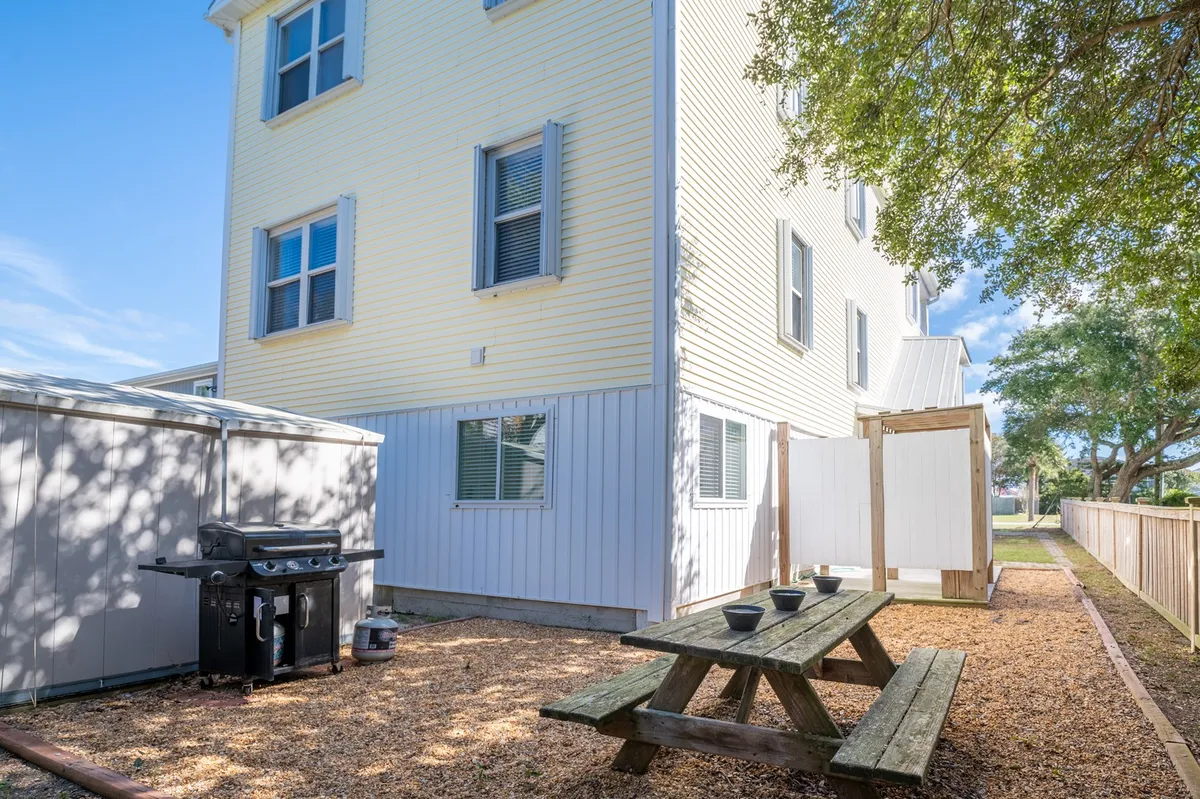 This exterior shot features a sunny picnic area with a picnic table, grill, a fenced area, and the building's exterior. The atmosphere is casual and family-friendly, ideal for outdoor gatherings or letting a dog relax in a safe space.