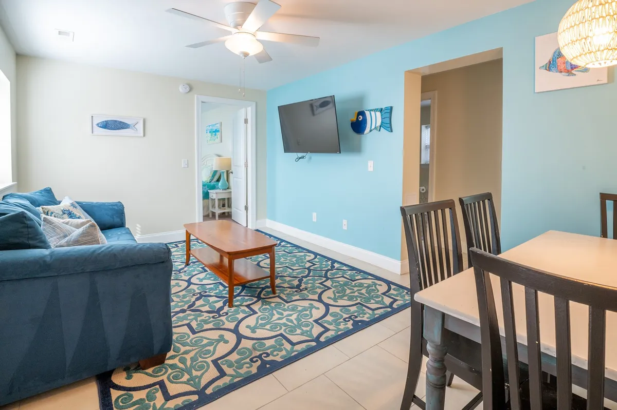 This image features a blue sofa paired with a decorative rug, a wooden coffee table, a dining table, and a wall-mounted TV. The layout is efficient, with all key elements of a living room within close proximity, evoking a sense of casual comfort. The setup suggests a space for movie nights, shared meals, and relaxed conversations.